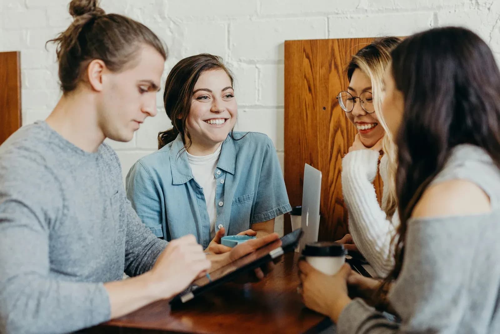 Four university students laughing around a table with a tablet and a laptop